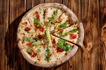 Pizza with salmon, mozzarella, cherry tomatoes, arugula, lemon and parmesan. Italian cuisine on a woden background