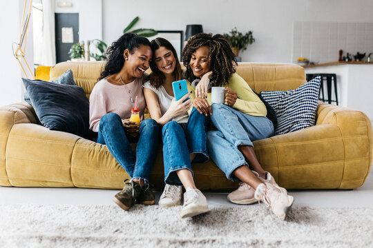Three happy multiracial young women friends having fun using mobile phone. Multi-ethnic group of female student enjoying free time sharing funny pictures on social media app. Female friendship concept