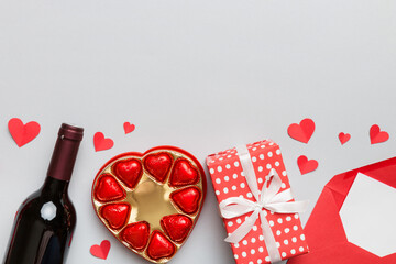 Bottle of red wine on colored background for Valentine Day with gift box, envelope and chocolate. Heart shaped with gift box of chocolates top view with copy space