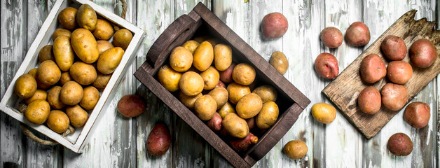 Yellow potatoes in the box and on the tray and red potatoes on the cutting Board.