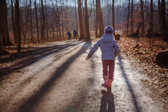 Child walks on sunlit tree-lied path with family in woods