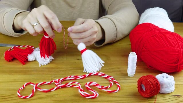 Woman making handmade traditional martisor, from red and white strings with tassel. Symbol of holiday 1 March, Martenitsa, Baba Marta, beginning of spring in Romania, Bulgaria, Moldova