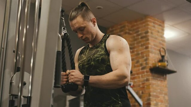 Muscular trainer doing cable triceps pushdown gym machine