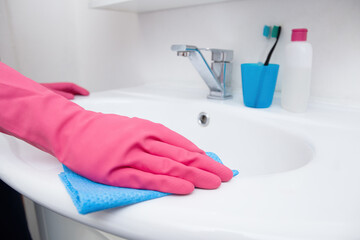 Home cleaning in the bathroom. A woman in pink gloves cleaning a white sink with a sponge and spray and detergent. Hygiene at home, house cleaning, keeping clean.