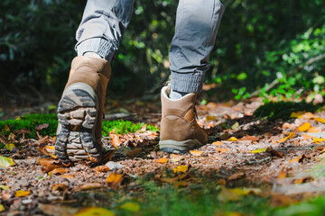 Unrecognizable male traveller or hiker walking in the forest and climbing on hill. Closeup hiking boots from the back side.