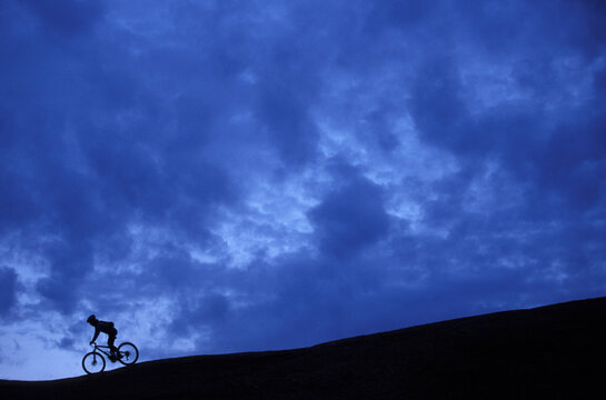 A silhouette of a woman mountain biking in the desert on slick rock.