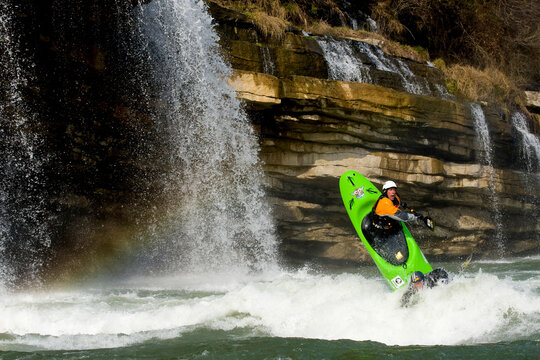 Two male kayakers paddling around waterfalls in a two person kayak.