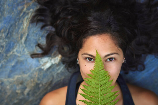 Woman with a fern on her face. She's lying on a rock and covers half her face with a fern leaf.