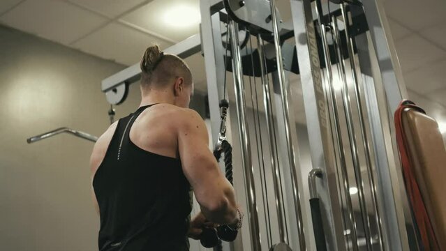 Muscular trainer doing cable triceps pushdown gym machine