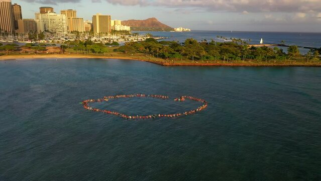 Aerial Forward Shot Of Tourists Gathering Circle With Surfboards On Sea In City Under Clouds - Oahu, Hawaii