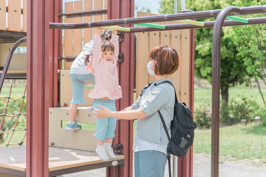 公園の遊具・雲梯（うんてい）で遊ぶ・運動する子供とママ（女の子・幼児・園児）
