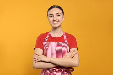 Obraz premium Beautiful young woman in clean striped apron on orange background