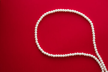Chat message bubble made of pearl jewellery necklace on red background.