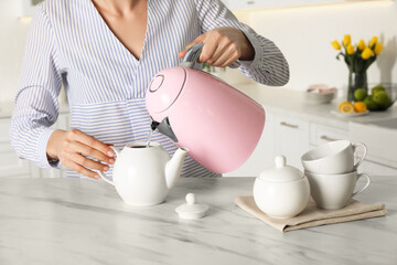 Woman pouring hot water from modern electric kettle in cup indoors, closeup