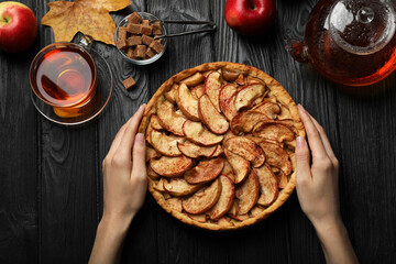 Woman with delicious apple pie at black wooden table, top view