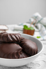 Delicious chocolate covered zephyrs in bowl on light grey table, closeup