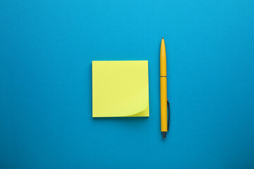 Paper note and pen on blue background, top view