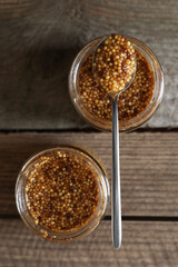 Jars and spoon of whole grain mustard on wooden table, flat lay