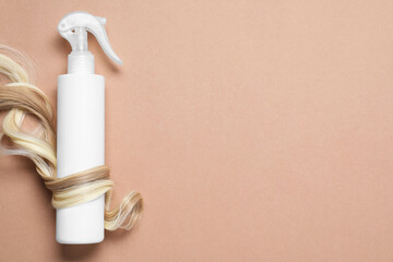 Spray bottle with thermal protection wrapped in lock of blonde hair on beige background, flat lay....