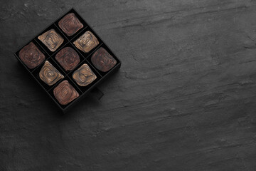 Box of tasty chocolate candies on black table, top view. Space for text