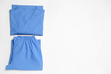 Fototapeta premium Light blue medical uniforms on white background, flat lay. Space for text