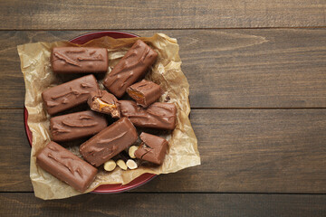 Many tasty chocolate bars with caramel and nuts on wooden table, top view. Space for text