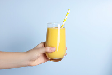 Woman holding glass of tasty smoothie on light blue background, closeup