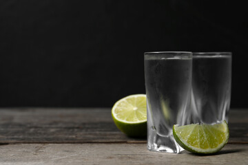 Shot glasses of vodka with lime on wooden table. Space for text