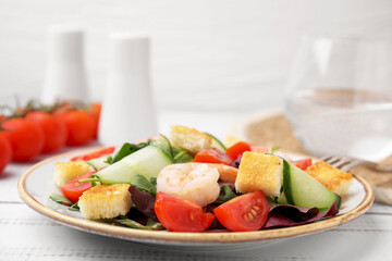Tasty salad with croutons, tomato and shrimps on white wooden table, closeup