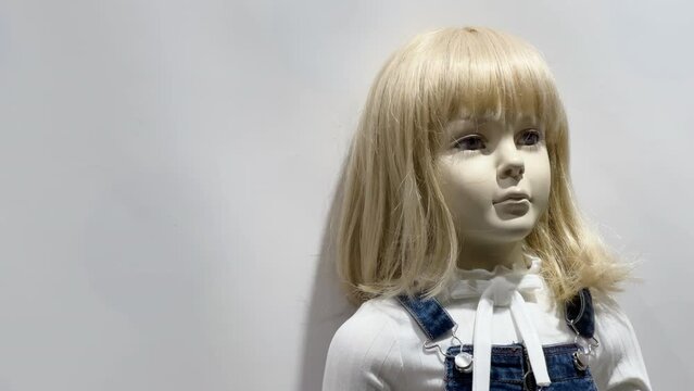 Mannequin of a girl with blond hair and in a denim overalls stands in the window of a children's clothing store. White background