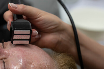 Elderly woman receiving radiofrequency lifting procedure for face skin rejuvenation and anti-age at aesthetic cosmetology center. RF lifting in beauty clinic.