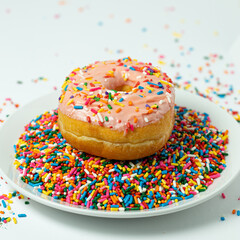Pink donut with sprinkles on plate of sprinkles 
