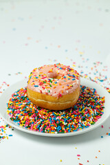 Pink donut with sprinkles on plate of sprinkles 