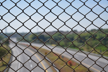 Fototapeta premium Chain link fence on flyover with highway blur background