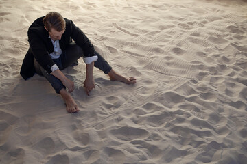 sad financier is frustrated, a young man with big plans is faced with a global economic crisis, concept. businessman in a suit is sitting on a pile of sand