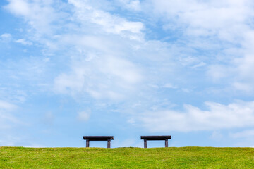 Public bench seat on green grass slope in Ang Kaew reservoir with cloudy blue sky background