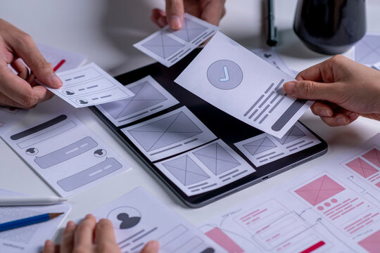 Close up ux developer and ui designer brainstorming about mobile app interface wireframe design on table.