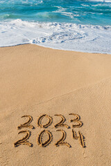 2023 2024 written in the sand with wave washing up- New Year concept