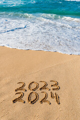2023 2024 written in the sand with wave washing up- New Year concept
