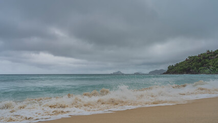A wave of turquoise ocean foaming on the beach. The spray is flying in the air. Water is mixed with...