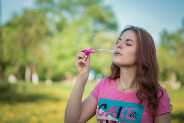 A young beautiful girl blows soap bubbles in nature.