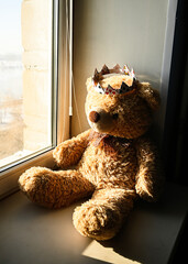 Fluffy brown teddy bear, sitting on the window.