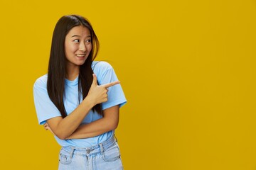 Fototapeta premium Asian woman smile with teeth hand gestures, signs and symbols on yellow background in blue t-shirt and jeans