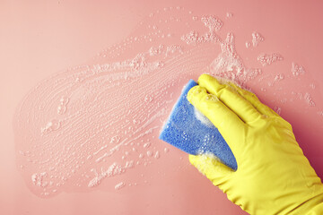 a hand in a shopping glove wipes soap suds from a pink background with a sponge