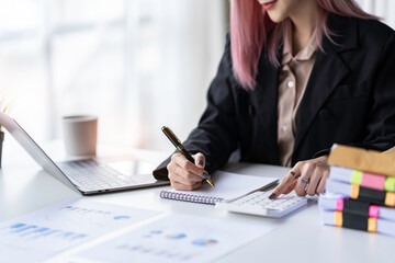 Portrait of an Asian businesswoman Calculates turnover by calculator Take notes to make financial reports or company profits.