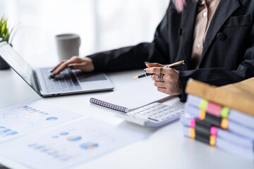 Portrait of a young Asian businesswoman sitting at a desk in an office recording data on a laptop. financial calculation and online delivery orders.