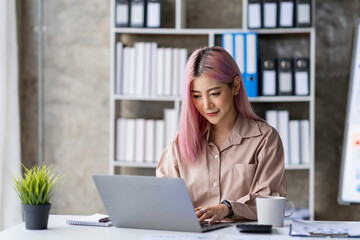 Portrait of a young Asian businesswoman sitting at a desk in an office recording data on a laptop. financial calculation and online delivery orders.