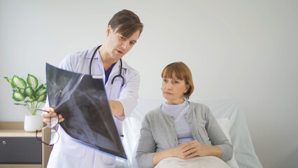 Portrait of caucasian doctor showing bone x-ray scan film of sick old senior elderly patient on bed in hospital in medical and healthcare treatment at nursing home. People lifestyle