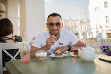 a young spanish man has breakfast in a cafe on the street on a summer day, a happy young guy eats a cake and drinks tea in a cafe