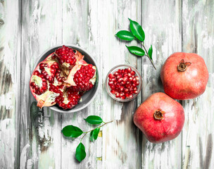 Grains and pieces of pomegranate in a bowl and whole pomegranates with leaves.